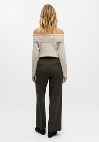 Beige schulterfreier Pullover, kombiniert mit dunkelgrünen, taillierten Hosen mit Knopf und Gesäßtaschen, getragen mit schwarzen Schuhen.