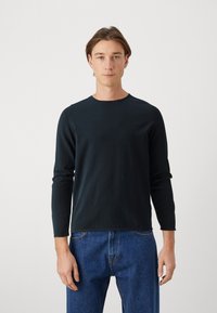 Czarna koszula z długim rękawem i okrągłym dekoltem uszyta z ciemnonawigacyjnej bawełny. Gładka tekstura, dopasowany krój i minimalne detale szycia. W zestawieniu z niebieskimi dżinsami.