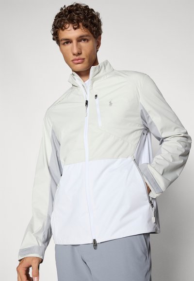 Lightweight, white jacket with gray accents. Features a zip front, high collar, and pockets. Smooth texture and athletic fit. Logo on chest.