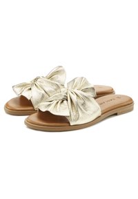 Gold metallic slide sandals with a large bow detail at the top, featuring a smooth texture and a tan leather footbed. Flat sole design.