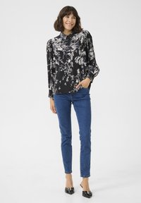 Zwarte blouse met bloemenprint, knoopsluiting aan de voorkant en lange opgezette mouwen. Gecombineerd met blauwe skinny jeans en zwarte hakken.