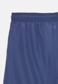 Mørkeblå shorts laget av glatt syntetisk materiale med elastisk midjebånd og forsterket bånddetalj på siden.