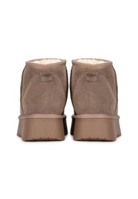 Botines de ante marrón con un suave forro de piel en color crema. Presentan una suela gruesa y texturada en marrón y detalles de costura en los laterales.