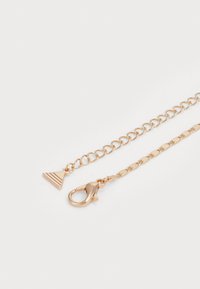 Collana in tono oro con ciondolo triangolare piatto a texture striata; la catena è composta da anelli ovali interconnessi e un gancio a molla.