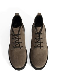 Braune Wildleder-Stiefeletten mit schwarzen Schnürsenkeln, runder Zehenform und schwarzer Gummisohle. Ausgestattet mit seitlichen Reißverschlüssen für ein einfaches An- und Ausziehen.