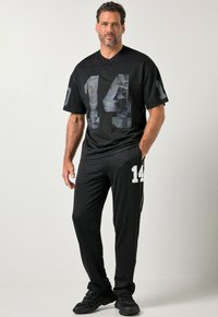 Musta urheiluasu, jossa on lyhythihainen paita, jossa on suuri maastokuvioitu numero 14, ja siihen sopivat housut, joissa on valkoinen numero 14.