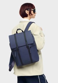 Navy backpack made of durable material, featuring a fold-over flap, black straps, and a front zipper pocket.