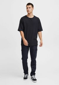 Czarna, oversize'owa koszulka z krótkim rękawem, zestawiona z ciemnymi spodniami cargo i czarnymi sneakersami z białymi akcentami.
