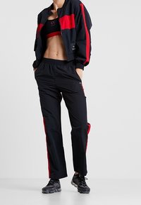 Zwart en rood sportoutfit bestaande uit een opstaande bomberjack met rits en gestreepte accenten, en broek met elastische tailleband. Gestructureerde stof en stijlvolle uitstraling.