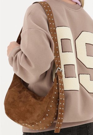 Bruine suède schoudertas met een gebogen ontwerp, met studs langs de riem en een ritssluiting. Casual gedragen aan de schouder.