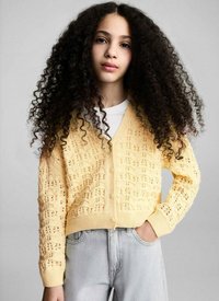 Gul stickad cardigan med ett strukturerat öppet mönster och knäppningar, i kombination med ljusgrå denimjeans.