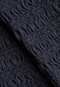 Tissu bleu foncé avec une texture froncée et plissée formée par des rangées horizontales de coutures élastiques créant un motif froncé et ondulé.