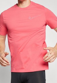 Korálové bavlněné tričko s kulatým výstřihem a krátkými rukávy. Na hrudi má reflexní logo Nike. Hladká textura, volný střih.