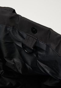 Interior em nylon preto com fecho de botão e anexo de laço. Apresenta textura suave e costura reforçada nas bordas.