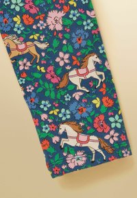 Tissu bleu avec des motifs floraux vibrants et des chevaux cabrés portant des selles roses dispersés sur le dessin.