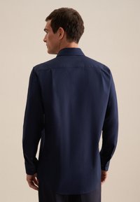Camicia a maniche lunghe blu navy con bottoni, dal tessuto morbido, con dettagli sul retro e polsini con bottoni, mostrata su un modello visto di lato.