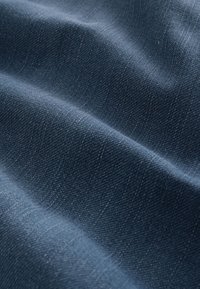 Tessuto denim blu scuro con trama diagonale visibile e pieghe morbide che creano ombre e luci.