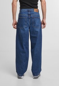 Jean en denim bleu foncé avec une coupe ample. Dispose de deux poches arrière, d'une étiquette en cuir au niveau de la taille et d'ourlets retroussés.
