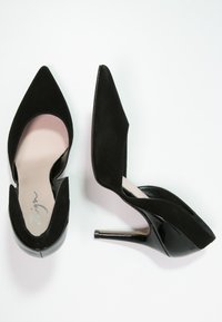 Černé vysoké podpatky se špičatou špičkou, vyrobené z nobukové kůže a lakované kůže, s výřezem po stranách a elegantním jehlovým podpatkem.