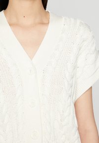 Weißer Strickcardigan mit V-Ausschnitt, kurzen Ärmeln, Knopfverschluss und Zopfmuster im gesamten Design.