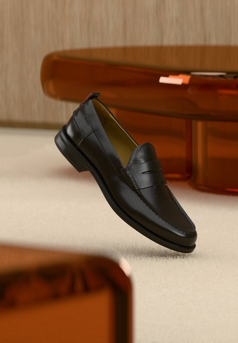 Schwarzer Penny-Loafer aus Leder, der über einem beigen Teppich schwebt, im Hintergrund unscharfe braune Holzmöbel.