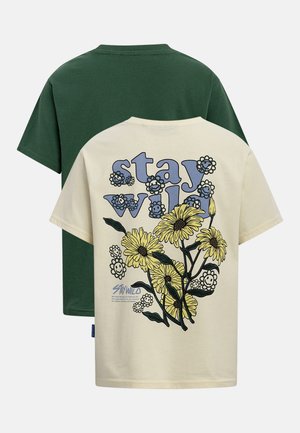 Deux t-shirts à manches courtes, l'un vert foncé et l'autre crème, avec le texte « stay wild » et un motif floral jaune avec des visages souriants au dos.