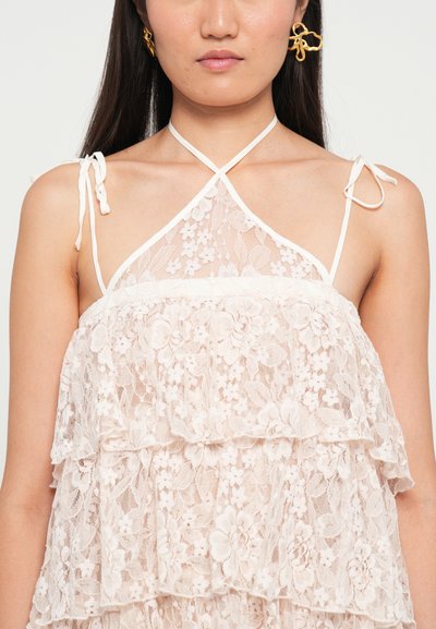 Kanten top met een gelaagd ontwerp, zachte beige kleur en delicate bloempatronen. Halterhals met verstelbare lintstrikken.