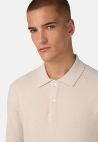 Strick-Poloshirt in hellbeige mit einer weichen Textur, klassischem Kragen und drei weißen Knöpfen am Hals.