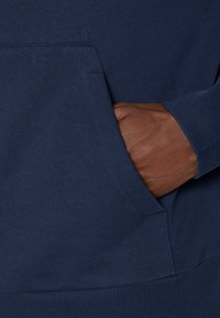 Navy blue sweatshirt featuring a front pocket with a ribbed cuff. The fabric has a smooth texture and is primarily solid in color.