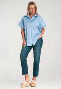 Jasnoniebieska koszula z krótkim rękawem zapinana na guziki z haftem kwiatowym, w parze z ciemnoniebieskimi dżinsami i beżowymi sandałami na platformie.