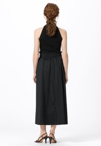 Svart halterneck-top i kombination med en lång, flödande svart kjol med resår i midjan, avslutad med svarta remsandaler.