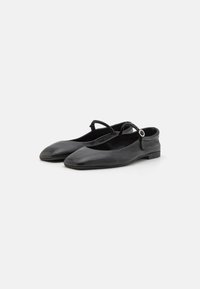 Black leather flats with a rounded toe, minimalistic design, adjustable strap with a circular accent, and low block heel.