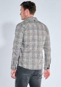 Herren-Langarmhemd mit kariertem Muster, in einem grau-beigen Farbschema, gefertigt aus strukturiertem Stoff mit Knopfdetails.