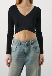 Black ribbed cropped top with long sleeves and deep V-neckline, paired with light blue high-waisted denim jeans featuring pockets.
