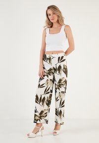 Witte crop top gecombineerd met hoge taille, wijde broek met een groen en zwart bladpatroon. Gladde stof met een getailleerde pasvorm.