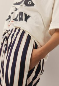 Tricou alb cu grafică și text negre, asortat cu pantaloni în dungi bleumarin și crem, având talie elastică și buzunare.