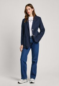 Blazer de rayas marineras de tejido suave con dos botones, combinado con una camiseta gráfica blanca y vaqueros rectos azules.