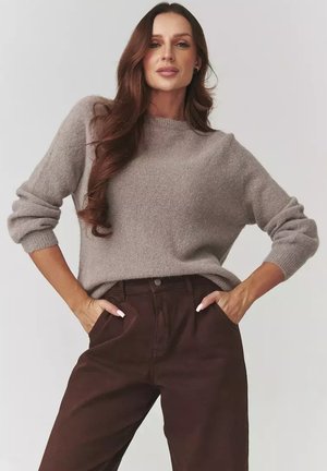 Brązowy sweter z wełny z okrągłym dekoltem i długimi rękawami w połączeniu z ciemnobrązowymi spodniami. Tekstura swetra wydaje się miękka, a fason luźny.