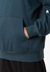 Donker teal sweatshirt met een kangoeroezak, ribgebreide boorden en onderrand. Gemaakt van zacht materiaal met een gladde textuur.