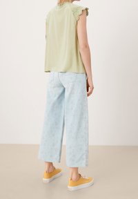 Top sin mangas color verde claro con borde de encaje, combinado con jeans de pierna ancha azules claros con un patrón floral, y zapatillas amarillas.
