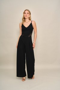 Svart jumpsuit med blonder på sidene ved midjen, V-utringning og vide ben. Glatt tekstur; kombinert med gulltilbehør.