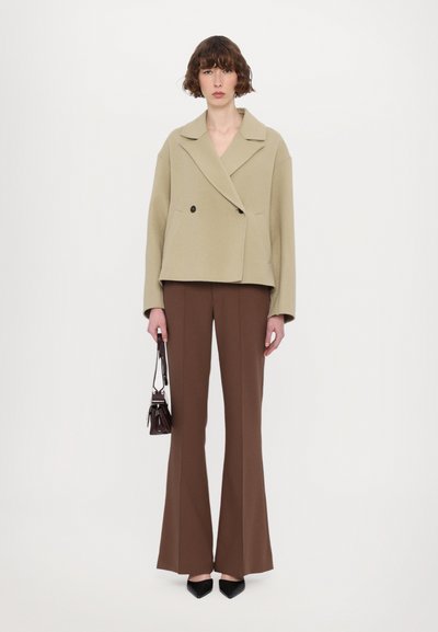 Manteau court beige à double boutonnage avec deux boutons noirs, associé à un pantalon brown évasé et un petit sac à main noir.