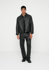 Chaqueta de cuero negra con cuello, cierre de cremallera y pantalones de cuero negro a juego. Textura suave, diseño minimalista y corte relajado.