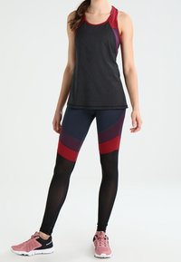 Czarna i burgundowa sportowa bluzka na ramiączkach z siateczkową teksturą, zestawiona z dopasowanymi legginsami w granatowe, burgundowe i czarne paski, dopełniona różowymi trampkami.