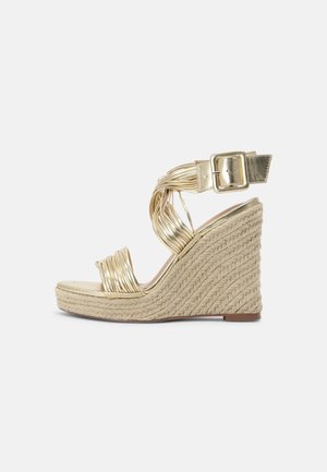 Sandale compensée dorée avec design à brides tressées, talon habillé de textile et fermeture à boucle. Semelle lisse et talon compensé texturé pour une bonne stabilité.