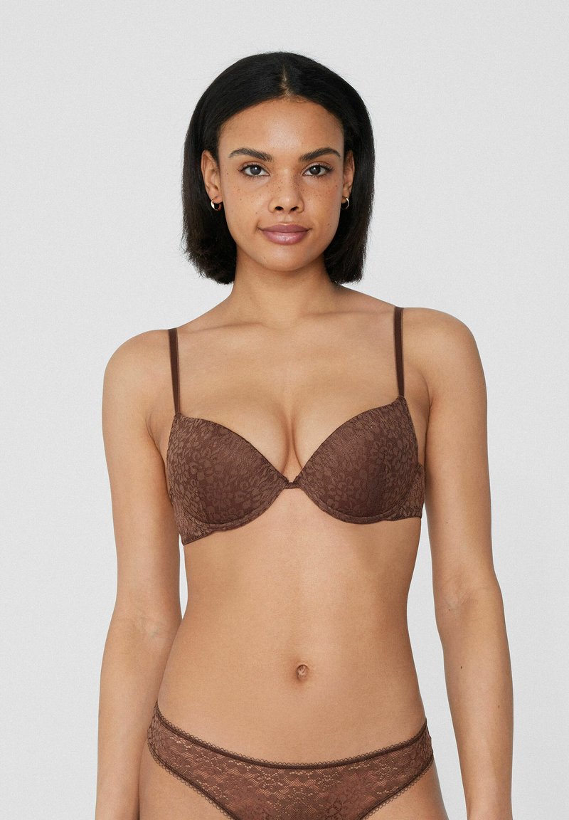 Hnědá krajková podprsenka s hlubokým výstřihem, tenkými nastavitelnými ramínky a květinovým vzorem; měkká textura s bezešvými košíčky.
