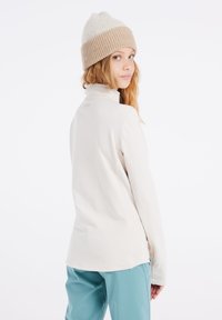 Lichtbeige lange mouw top met een hoge kraag, voorzien van een subtiele merklogo op de achterkant en een gladde, rekbare stof.