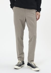 Világosszürke nadrág finom textúrával, egyenes szabással, sima elülső résszel és oldalsó zsebekkel, fekete sportcipővel párosítva.