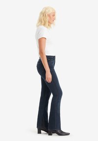 Mörkblå utsvängda jeans med medelhög midja, fram- och bakfickor samt en liten spricka i fållen, kombinerat med en åtsittande vit t-shirt.