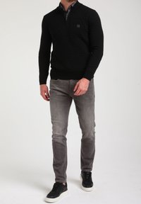 Mustapipoinen neulepaita, jossa on puolivetoketju, kohotettu timanttikuosi, yhdistettynä harmaisiin farkkuihin ja mustiin lenkkareihin, joissa on valkoiset pohjat.